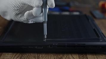 A person is using a screwdriver to remove a screw from a laptop video