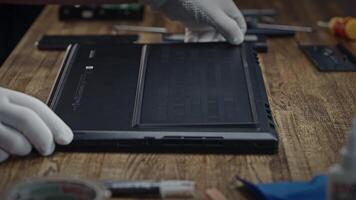 A person in white gloves is interacting with a laptop on a hardwood table. Disassembling a modern laptop for cleaning and maintenance. Troubleshooting video