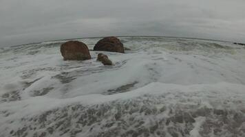 Black Sea, waves with white foam during a storm roll on a sandy beach, rocks on the shore video