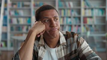 Bored unhappy African American man library student learn study negative educational university dissatisfied male displeased guy boredom tired lazy college disappointed pensive weary fatigue bookshelf video