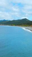 Top view of coastline of coast with mountains on horizon. Clip. Island with green forest and mountains on ocean coast. Paradise place to relax in wild on coast of island with mountains video