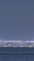 Turkey, Istanbul-December, 2020. Timelapse of luminous bridge. Action. Coast and bridge glow with bright lights with passing boats in evening. Evening harbor in lights and with many passing boats video