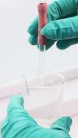 Close up of transparent liquid being poured into a bottle with a pipette on a white background. Clip. Hands in gloves pressing on a pipette. video