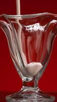 Close-up of yogurt in glass cup on red background. Stock footage. Fresh yogurt is poured into clear glass. Stream of smoothies fills glass on isolated background video