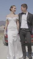 Newlyweds are walking beautifully in field. Action. Stylish newlyweds are hugging on road. Newlyweds in stylish outfits are walking epically along field road video
