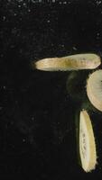 Slices of kiwi fruit drop into water full of bubbles in slow motion. Action. Close up of cut tropical fruit falling underwater isolated on black background. video
