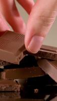 Close up of hand taking a piece of milk tasty chocolate lying on the table. Stock footage. Broken chocolate bar isolated on beige background, concept of sweets and confectionary. video