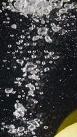 Close-up of whole lemon falling into water. Action. Whole lemon falls into water with bubbles on black background. Refreshing lemon drops into water video