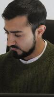 Man is working intently at laptop in office. HDR. Handsome man is working at laptop in sweater. Freelancer or writer working on laptop video