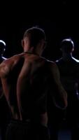 Rear view of a muscular male fighter standing in a dark room against for man silhouettes, unequal confrontation. Stock footage. Four enemies hidden in the shadow, concept of fight with yourself. video