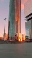 A small square in front of a modern glass facade business center with a golden sunset reflected in windows. . Concept of modern architecture. video