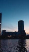 Beautiful landscape with a flowing river and blue sky getting darker at the sunset with a city on the background. . Timelapse effect of a city with skyscrapers located along the river. video