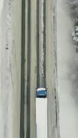 Aerial view of traffic on the road passing through the winter forest in severe weather. Scene. Top view of a cargo truck moving on a straight road surrounded by snow covered woods. video