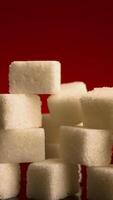 Close up of growing pile of sugar cubes isolated on dark red background. Stock footage. Stop motion effect, concept of the sugar increasing consumption. video