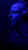 Concept of song writing and creativity. HDR. Close up side view of an enthusiastic young male musician in earphones singing in microphone in sound recording studio booth. video