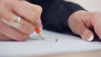 Woman's hand with a beautiful ring of a designer is drawing sketch of dress in atelier. Female tailor draws with a sharp pencil on the table. Close-up video