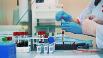 Two nurses are working with test tubes in medical laboratory. Scientists women in gloves fill the vials with liquid and put them into a rack on a sterile table. video
