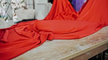 Seamstress laying out beautiful red cloth on a wooden table. Work place table of tailor in workshop and a big piece of red fabric indoors. video