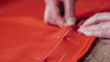 Professional seamstress puts the pins into the red fabric on the table. Woman's hands at work with red cloth and pins in the workshop. Close-up. video