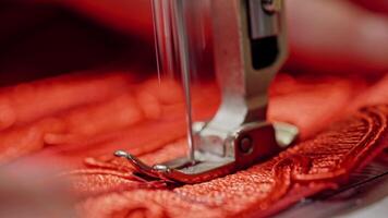 Steel part of sewing machine with a needle working on red cloth. Seamstress woman is sewing on modern machine with red fabric. Close-up video
