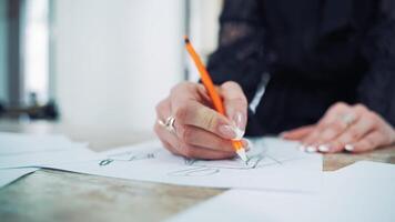 Process of drawing a sketch of a model dress on paper by female tailor. Professional designer draws with a pencil on the table in atelier. video