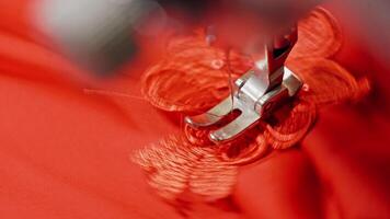 Sewing process on red fabric making a design with a beautiful flower. Hands of seamstress are holding material while working on sewing machine. Close-up. video