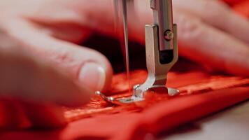 Process of sewing machine working with red fabric. Woman's hands at work on metal sewing machine with bright red material. Close-up video