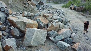 Active tourist climbing on a big pile of stones in the mountainous area. Scenic view of rocky cliff and a young man hiker walking on that place. Camera moves up. video