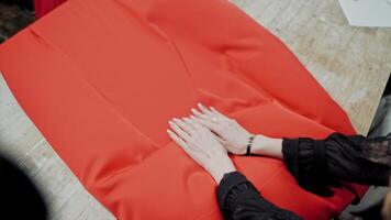 Femile tailor is layng out bright red fabric on the wooden table. Large piece of red material in the hands of a seamstress in workshop. video