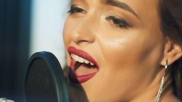 Profile of a beautiful girl's face with perfect makeup singing in the sound studio. Young singer emotionally recording new song. Lady sings into microphone. Slow motion Close-up video