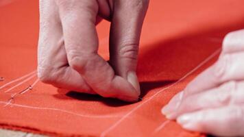 Female hands of the skilled worker putting the pin to the fabric. Red cloth with white lines and a tailor pinning the material on the table. Concept sewing and handicraft. video