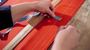 Female's hands are sketching lines with a tape measure and a soap on a table. Sewer works with red fabric and a ruler in atelier. Handicraft concept. video