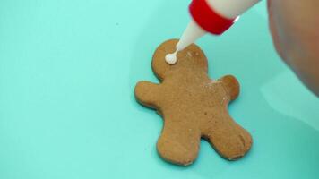 Unrecognizable hands paint the Gingerbread boy with white cream. Hands painting gingerbread cookie on the blue background. Close-up video