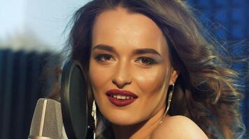 Passionate model is singing next to the microphone iin the sound studio. Close-up face of beautiful singer woman with perfect makeup at mic looking at camera. video