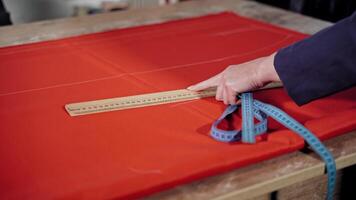 Female tailor is drawing sketch lines with a soap and a ruler on red fabric. Preparing details of material for new, modern dress or other clothes. Feminine hobby. video