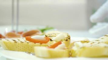Work of a professional chef for the preparation of traditional canapes. Process of preparation toasts with cheese, tomato and becon on the plate in the restaurant. video