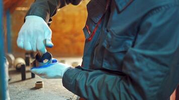 Male worker uses a brush to paint a circle tool for a special section of a machine. Man in working clothes paints in blue color details in the manufacturing hall. Close-up video