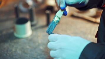 Close-up of man's hands with a brush painting metal tool with blue color in factory. Male worker in gloves paints instruments at workshop. video