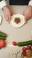 Cook shows the finished tartare. It consists of raw beef or veal meat and sour cream sauce. It is served with herbs and onions. You can add other ingredients to it. Top view video