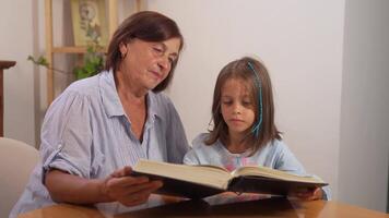 Smiling girl going through book with grandmother on table at home video