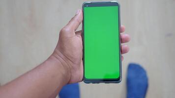 A hand holding a smartphone device with a green screen, suitable for display or editing purposes video