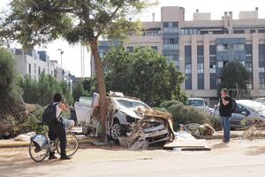 VALENCIA, SPAIN OCTOBER 31, 2024. Journalists documenting the aftermath of a flood in Valencia, with a wrecked car entangled in debris and a tree photo