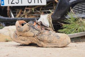 VALENCIA, SPAIN OCTOBER 31, 2024. A mud caked work boot lies abandoned near a damaged car, highlighting the devastating impact of the recent floods in Valencia photo