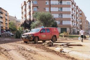 VALENCIA, SPAIN OCTOBER 31, 2024. Red emergency vehicle driving through thick mud on city street after devastating flood in Valencia, Spain photo