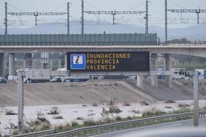 VALENCIA, SPAIN OCTOBER 31, 2024. Electronic road sign warning about floods in Valencia, Spain, with a flooded riverbed in the background photo