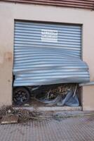 VALENCIA, SPAIN OCTOBER 31, 2024. Broken garage door revealing a damaged car, consequence of the devastating floods in Valencia photo