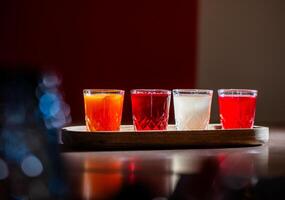 Four colorful shots of alcoholic beverages are placed on a wooden tray, creating a vibrant and inviting scene photo