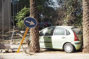 VALENCIA, SPAIN OCTOBER 31, 2024. Showing the aftermath of a devastating flood in Valencia, with a damaged car stuck between palm trees and debris scattered around photo
