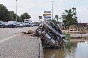 VALENCIA, SPAIN OCTOBER 31, 2024. Devastating consequences of flooding in Valencia, with a destroyed car lying on the roadside photo