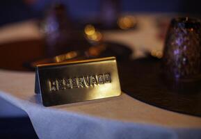 Golden reserved sign placed on restaurant table, indicating a prior booking, amidst ambient lighting and table settings photo